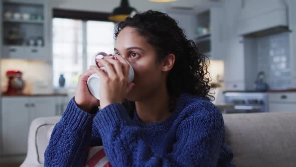 Mixed race woman sitting on couch and drinking coffee alt
