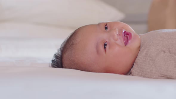 An Asian newborn baby is laying down on a soft white sheet mattress. Starring at his parents and fee alt