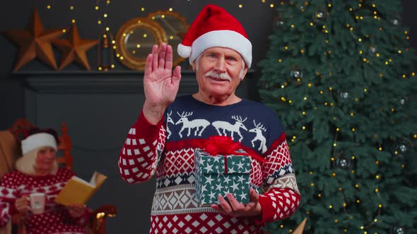 Senior Grandfather in Christmas Sweater Smiling Friendly at Camera and Waving Hands Gesturing Hello alt