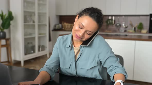 Woman Talks on the Smartphone and Takes Notes with Pen Using Laptop for Remote Work