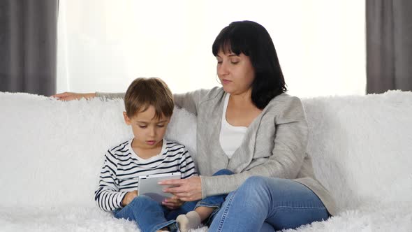 Happy Family: Mother and Son Spend Time Together Playing or Watching a Movie on a Tablet. The alt