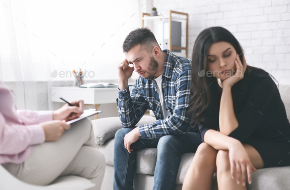 Stressed couple sitting separately at family counselor office