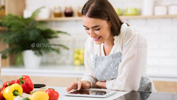 Looking for favorite recipe. Woman using digital tablet at kitchen