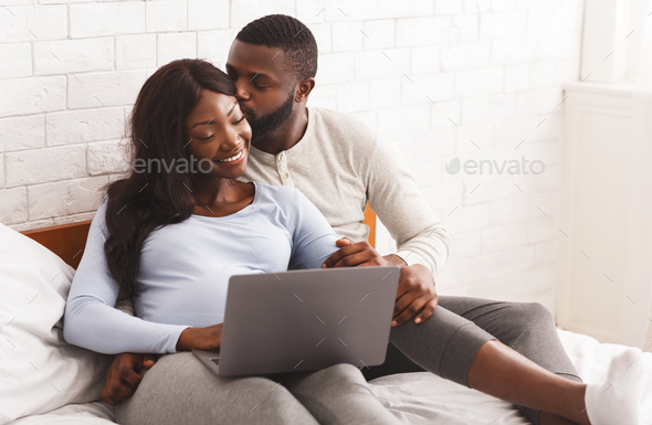 Pregnant girl and her husband using laptop, laying on bed - Stock Photo - Images