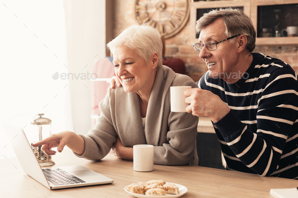 Retired couple browsing on laptop, enjoying tea at kitchen
