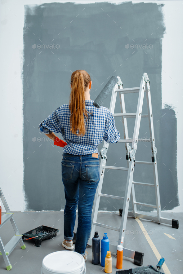 Female house painter looking on wall, back view - Stock Photo - Images