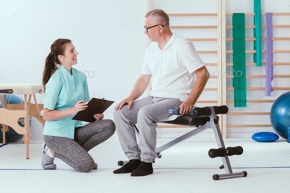Injured older man and a young professional physiotherapist prepare for gym exercises