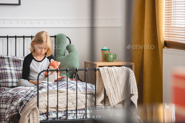 Cute little girl sitting on her single metal bed in trendy bedroom interior for child