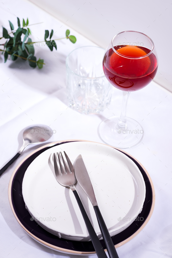 Tableware and decorations for serving a festive table. Plates, red wine glass and cutlery with green - Stock Photo - Images