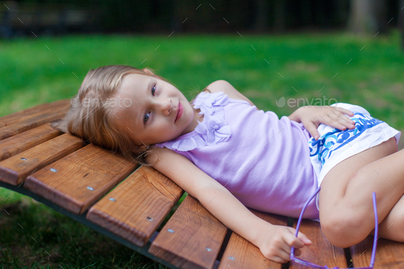 Cute Little Girl Lying On Wooden Chair Outdoor In The Park Stock Photo By Travnikovstudio