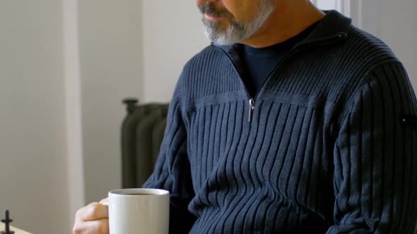 Man having coffee while playing chess in living room alt