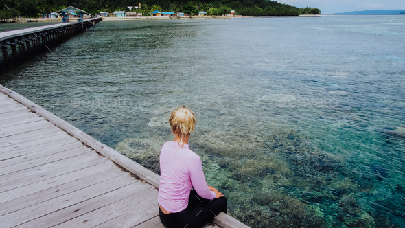 Girl on a wooden jetty near Yenbuba village leading to Mansuar island in Raja Ampat. Beautiful - Stock Photo - Images