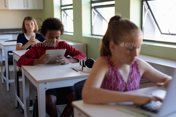 Group schoolchildren sitting at desks using personal computers