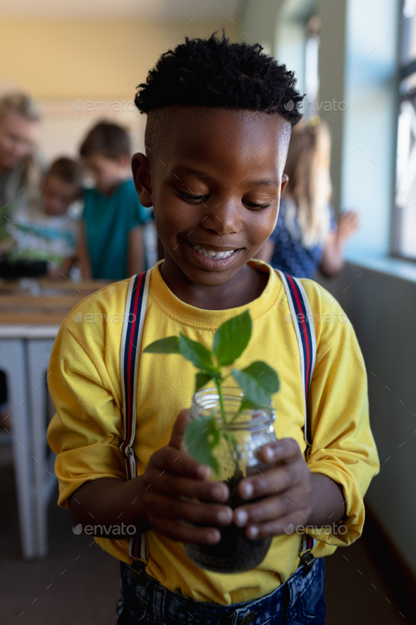 Schoolboy standing holding a seedling plant in a jar of earth in an ...