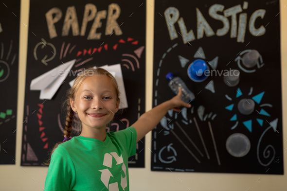 Schoolgirl wearing a green t shirt with a white recycling logo on it and it, pointing to a poster