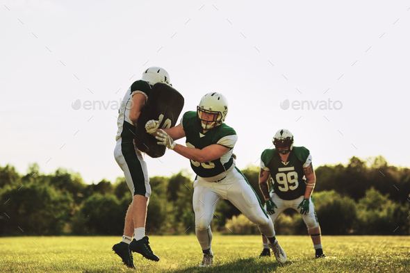 American football teammates practicing defensive tackles on a sports field
