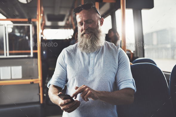 Smiling man with a beard sending texts on the bus