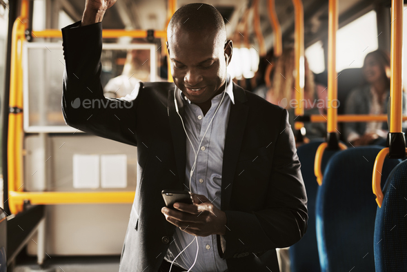 Smiling African businessman standing on a bus listening to music