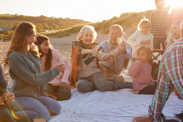 Multi-Generation Family Opening And Pouring Champagne To Celebrate At Winter Beach Vacation
