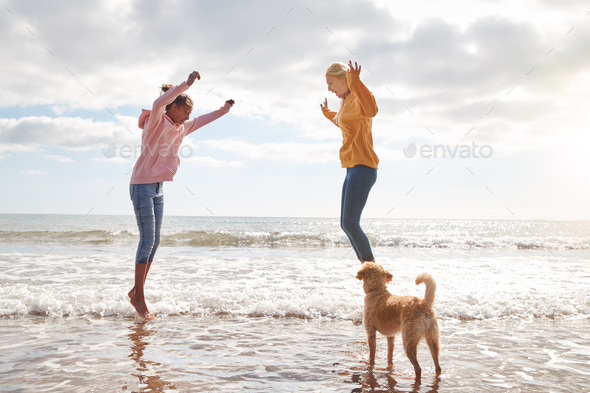 Mother And Daughter With Dog Jumping Over Waves On Autumn Beach Vacation