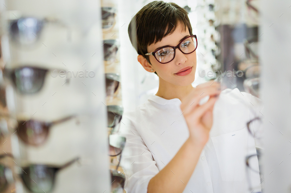 Pretty young woman is choosing new glasses at optics store