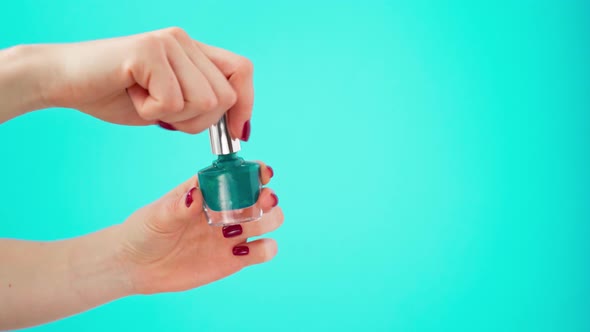 Female Hand Holding Bottle of Nail Polish Against Blue Background alt