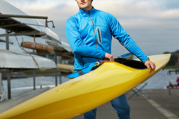 Male athlete in swimming sportswear carrying yellow kayak
