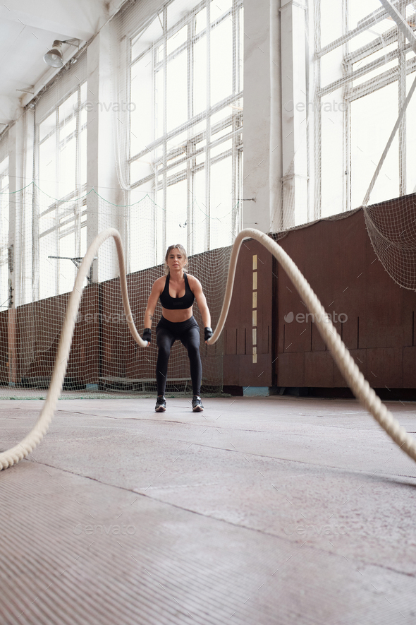 woman in black sportswear burning calories by doing exercise with ropes in gym
