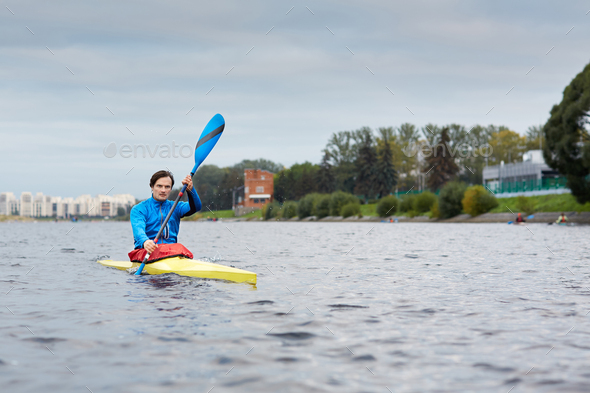 Professional Caucasian male athlete paddling along the river in yellow kayak