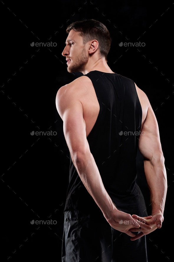 Rear view of young sportsman in black activewear exercising in isolation
