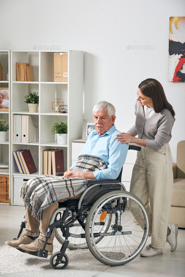 Young female care giver talking to senior male pensioner in wheelchair