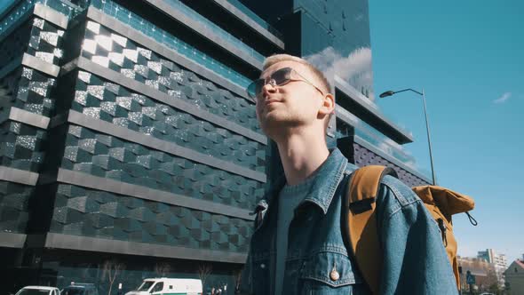 A Male Traveler with a Yellow Backpack Takes Pictures of the City on Camera alt
