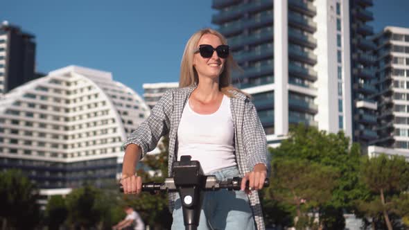 Young beautiful girl rides electric scooter in summer along street, alt