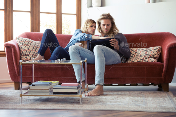 Lovely young couple drawing with they digital tablet while sitting on sofa at home. - Stock Photo - Images