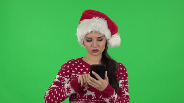 Portrait of Sweety Girl in Santa Claus Hat Is Angrily Texting on Her Phone. Green Screen alt