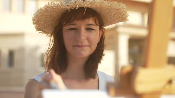 Portrait of Happy Inspired Female Painter in Straw Hat Smiling Making Paint Strokes in Slow Motion alt