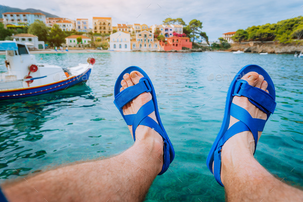 Man feet in sandals over blue water in front of the beautiful assos bay. Kefalonia Greece