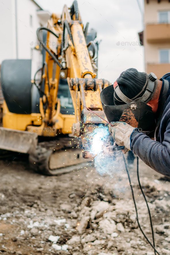 Professional welder with protection gear and mask welding broken excavator arm