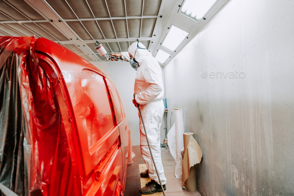 worker painting a red car in a special painting box, wearing a white costume and protection gear