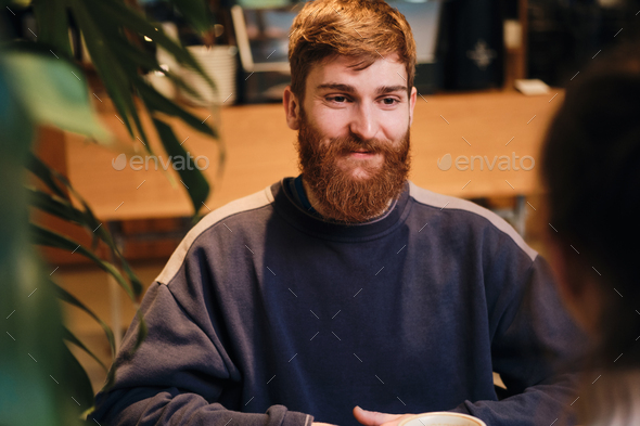 Young cheerful bearded man happily looking away on meeting in cozy cafe