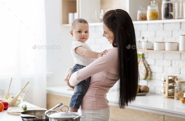 Adorable baby smiling at camera on mommy\'s hands at kitchen