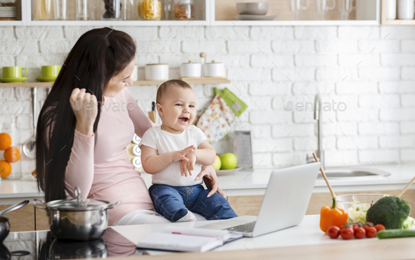 Positive woman enjoying success, working on laptop with baby