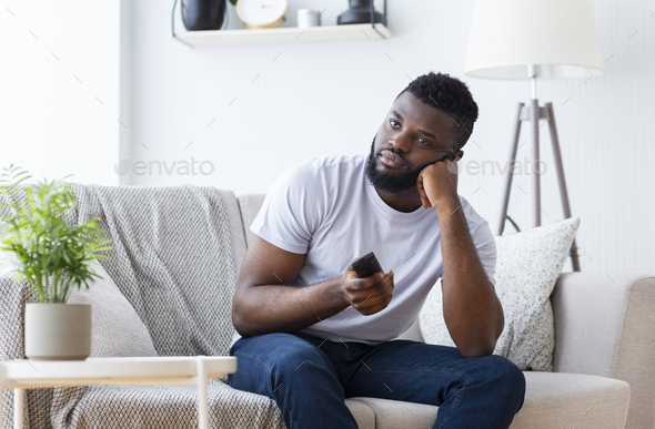 Bored african guy sitting at home, switching tv for film