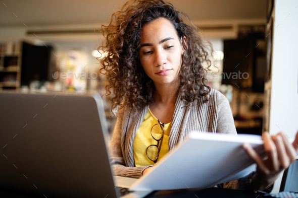 Young afro american woman sitting at table with books and laptop for finding information