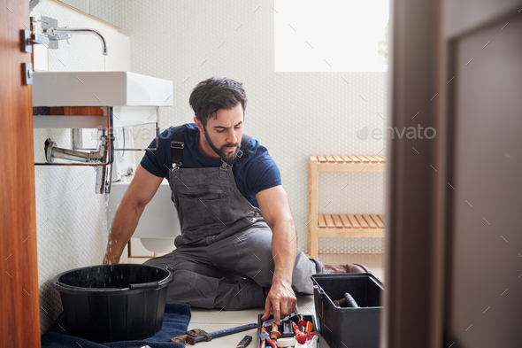 Male Plumber Working To Fix Leaking Sink In Home Bathroom
