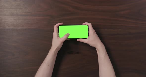 Top View Man Hand Using Smartphone with Green Screen Over Black Walnut Wood Table alt