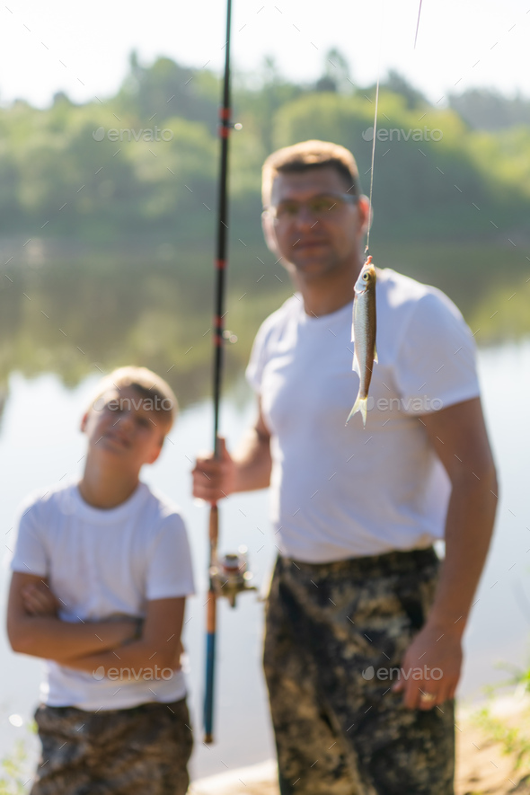 Such a small fish. Father and son stretching a fishing rod with fish on the hook while little boy