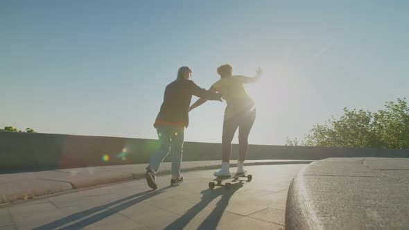 Rear View of Happy Females Learning to Ride Skateboard Outdoors at Dawn alt