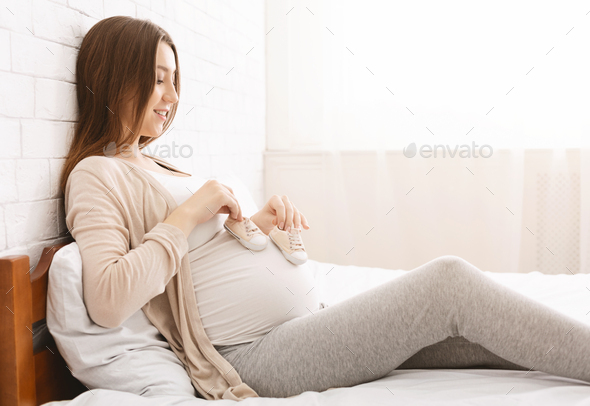 Happy pregnant woman playing with her belly and tiny boots