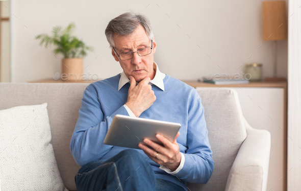 Serious Elderly Gentleman Using Tablet Sitting On Couch At Home
